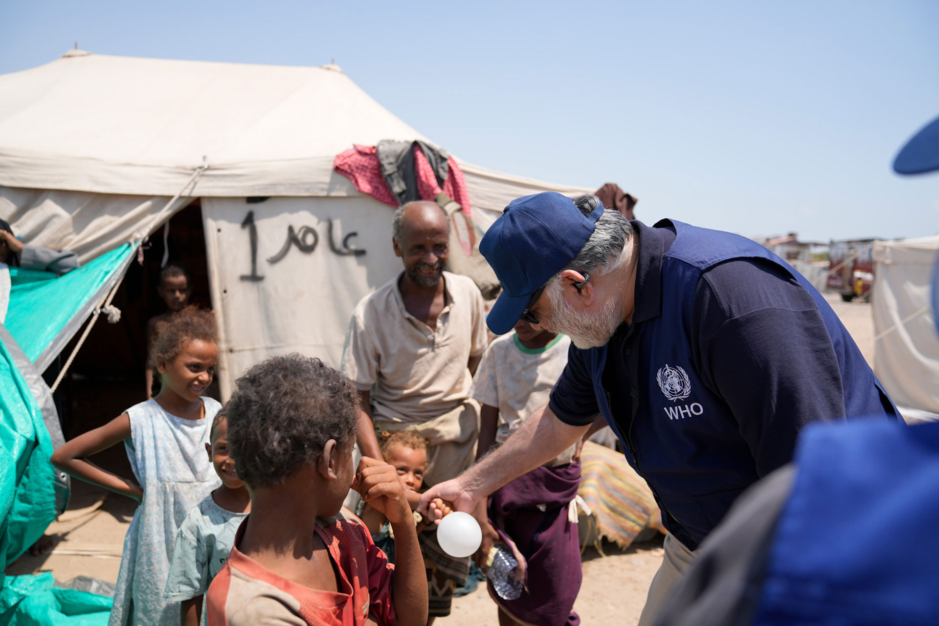 Dr Syed Jaffar Hussain greets children outside their family tent at Al-Firdous camp. Photo credits: WHO Yemen